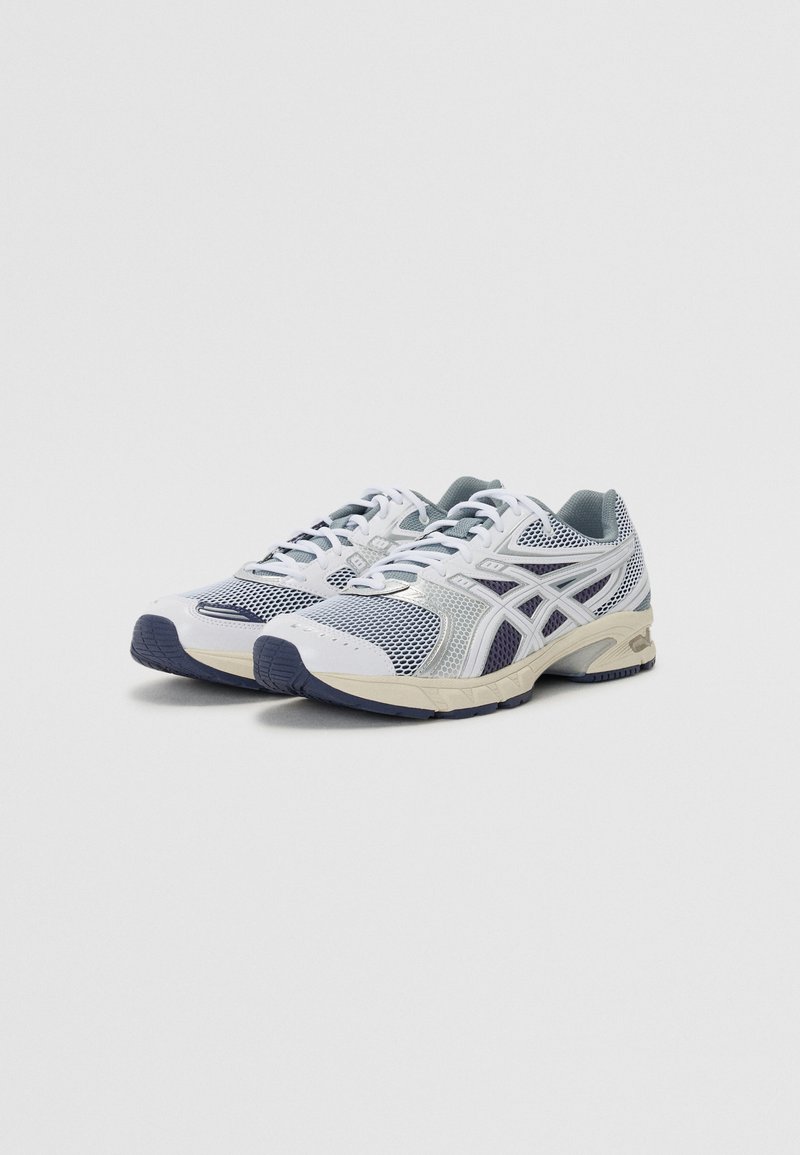 Zapatillas de correr en malla blanca y materiales sintéticos, con acentos en gris, una suela acolchada y un agarre texturizado en la parte inferior.