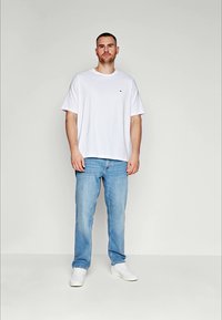 Biała bawełniana koszulka z krótkim rękawem i logo na piersi, połączona z jasnoniebieskimi dżinsami i białymi sneakersami. Prosty design, luźny krój.
