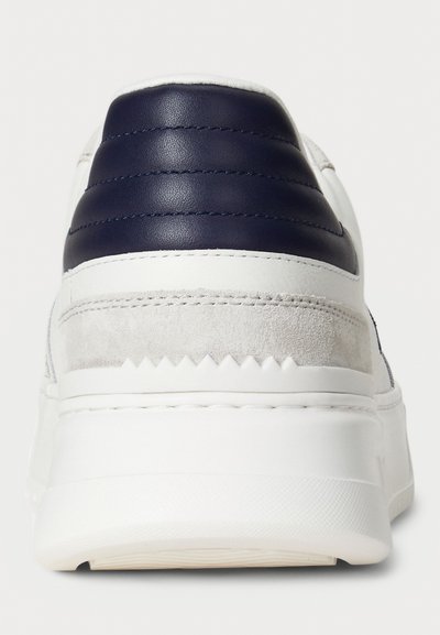 Vedere din spate a unei adidași albi cu o talpă texturată albă, accente din suede bej și guler căptușit de culoare albastru închis.