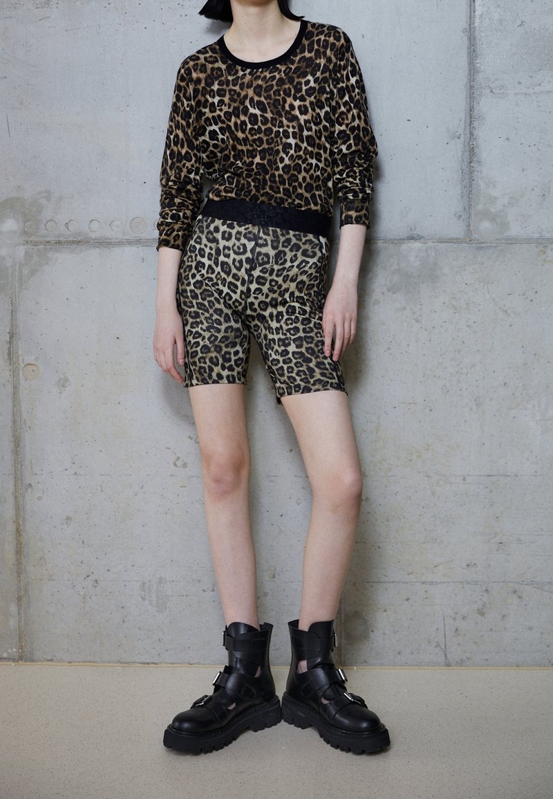 Bluzka z długim rękawem w panterkę i dopasowane szorty w beżowym i czarnym kolorze, zestawione z masywnymi czarnymi botkami na kostkę z paskami i grubą podeszwą.