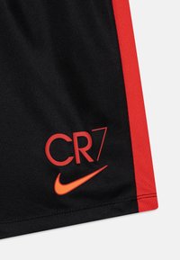 Pantalones cortos de deporte negros con una franja lateral roja, que presentan el texto "CR7" en rojo y un logo de Nike en naranja cerca del dobladillo.
