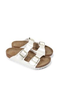 Sandales Birkenstock blanches avec deux boucles réglables, semelle en liège et semelle en caoutchouc. Texture lisse avec une finition mate.