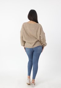 Beige gebreide trui met een losse fit en brede mouwen, gecombineerd met blauwe skinny jeans en transparante hoge hakken.