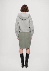 Sudadera gris con capucha combinada con una falda verde oliva, que presenta dos bolsillos traseros, y botas negras hasta la rodilla con tacón cuadrado.