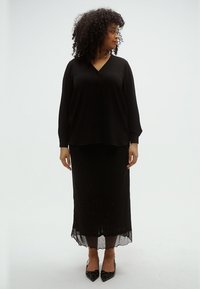 Μαύρο πουκάμισο με κουμπιά και μακριά μανίκια, σε συνδυασμό με μια μακριά φούστα με στρώσεις από μαύρα παγιέτες. Τα μυτερές μαύρες γόβες ολοκληρώνουν το σύνολο.