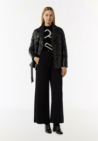 Schwarze gesteppte Lederjacke über einem schwarz-weißen gemusterten Pullover, kombiniert mit schwarzen weit geschnittenen Hosen und Ankle Boots.