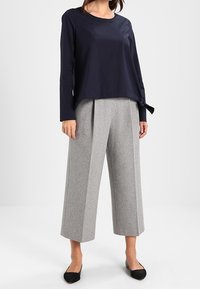 Marinblå långärmad topp med sidoknytning, tillsammans med högmidjade, vida grå byxor i strukturerad tyg, kompletterat med svarta flats.