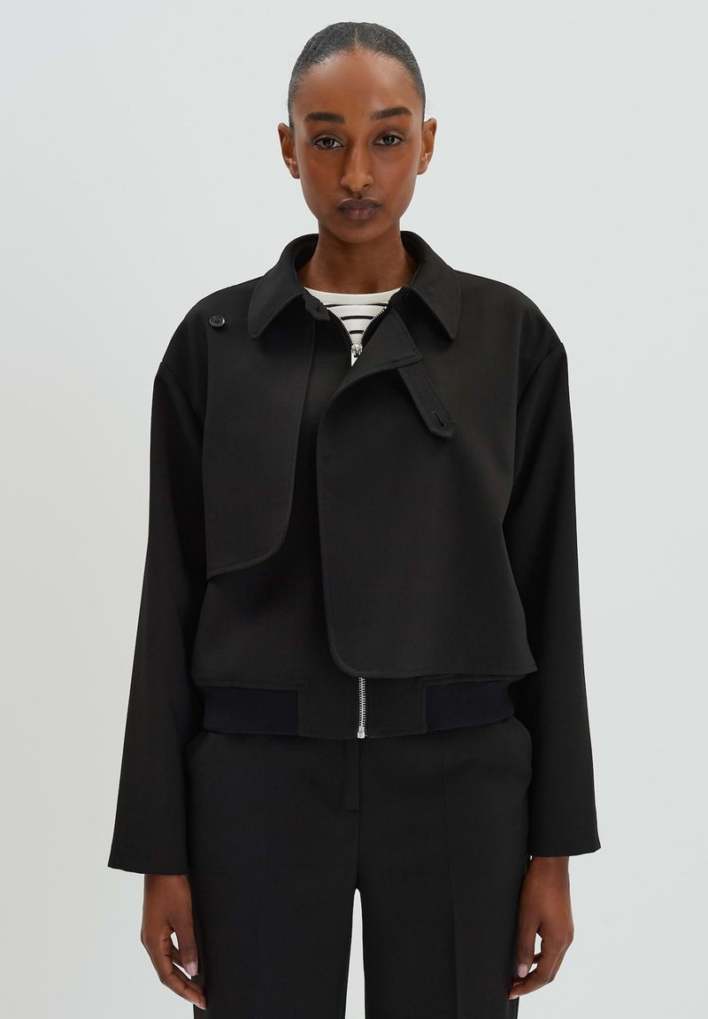 Zwarte cropped jas met een notch-kraag, een rits aan de voorkant en een knoopflapdetail. Kenmerkt een textuurstof en een geribde zoom.
