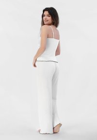 Top ajustado blanco sin mangas con tirantes finos y pantalones blancos fluidos. Los pantalones tienen un dobladillo festoneado. Textura suave y tejido ligero.