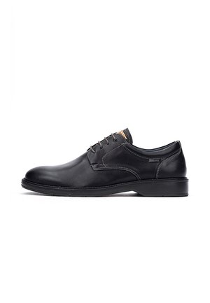 Chaussure habillée pour hommes en cuir noir avec bout rond, fermeture à lacets, surpiqûres contrastées et talon bas sur fond blanc.
