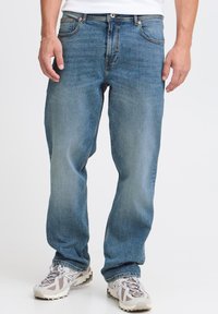 Jeans de mezclilla azul claro con un diseño de pierna recta, estilo de cinco bolsillos y un ligero desgaste. Combinados con zapatillas deportivas grises y beige.