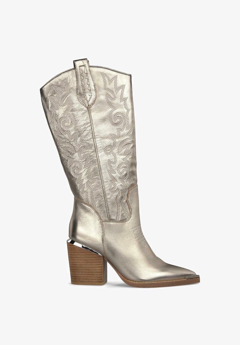 Metallisch silberner Cowboy-Stiefel mit spitzem Zeh, aufwendigem geprägtem Blumendesign und gestapeltem Holzabsatz. Verfügt über Ziehlaschen für einfaches An- und Ausziehen.