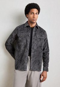 Chemise à boutons en velours côtelé gris foncé avec un motif floral, dotée de deux poches poitrine, de boutons métalliques et d'une coupe décontractée.