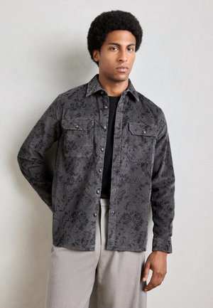 Button-up shirt in dark gray corduroy with a floral pattern, featuring two chest pockets, metallic buttons, and a relaxed fit.