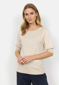 Pull en maille beige avec un col rond, des manches trois-quarts et des manches côtelées, associé à un pantalon bleu marine. Texture douce, design simple.