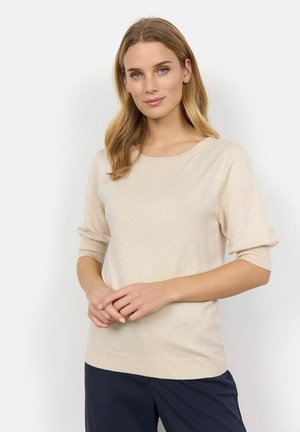 Pull en maille beige avec un col rond, des manches trois-quarts et des manches côtelées, associé à un pantalon bleu marine. Texture douce, design simple.