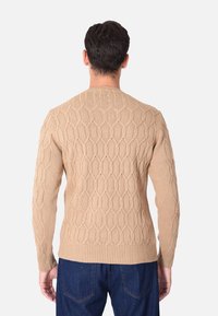 Maglione beige lavorato a maglia con un motivo a nido d'ape testurizzato, collo rotondo e polsini e orlo a coste. Progettato per una silhouette aderente.