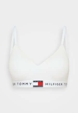 Hvit sømløs bralette med justerbare stropper og et bredt elastisk bånd med merkevare som har røde, hvite og blå logo aksenter.