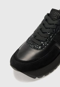 Sneaker noire avec une tige en daim, accents en textile brillant et détails texturés sur la pointe, semelle en caoutchouc épaisse et lacets plats.