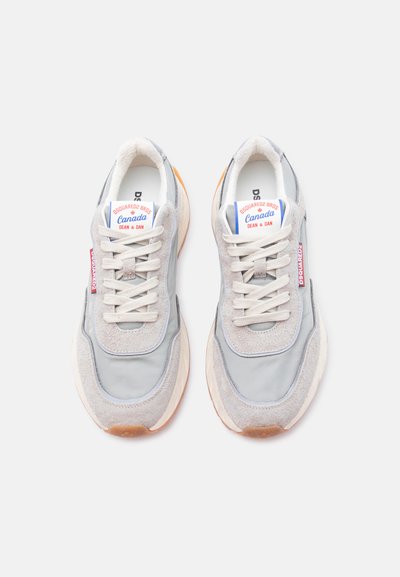 Paire de baskets en daim gris et beige avec des lacets blancs, une étiquette de marque sur le côté, et un label indiquant "Dsquared2 Bros Canada Dean & Dan" sur les languettes.