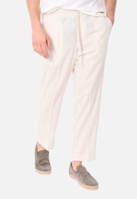 Pantaloni in lino beige chiaro con cintura elastica e cordino. Taglio a gamba dritta, superficie testurizzata, abbinati a scarpe grigie di tipo slip-on.