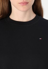 Felpa in cotone nera con collo tondo, caratterizzata da un piccolo logo in rosso, bianco e blu sul lato sinistro del petto.