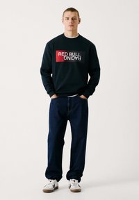 Námornícky sveter s logom "RED BULL RACING" v červenej a bielej farbe. V kombinácii s tmavými džínsami a bielymi teniskami. Ležérny strih, rebrované manžety.