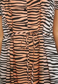 Šaty na knoflíky se vzorem zebry v černé a oranžové barvě, se staženým pasem a zavázáním, vyrobené z lehkého materiálu.