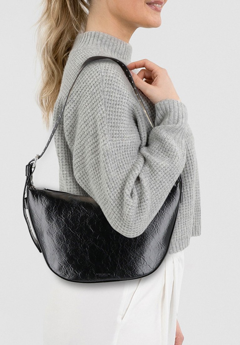 Borsa a spalla nera in pelle sintetica con forma curva, texture sottile e tracolla regolabile, indossata con un maglione grigio in maglia.