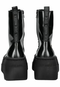 Botines de charol negro con plataforma gruesa, cierre de cremallera y tacón con logotipo grabado. Cuenta con una lengüeta para facilitar el calzado.