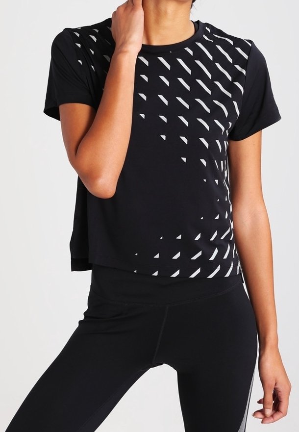 Musta urheilupaita, jossa on cropped-muotoilu ja valkoisella ylävasemmalla puolella oleva teksturoitu geometrinen kuvio. Yhdistetty mustiin leggings-housuihin.