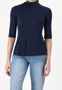 Navy blue fitted top with a high neckline, half sleeves, and a pleated design at the waist, made from a smooth, stretchy fabric.
