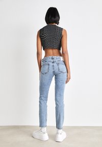 Svart kortärmad topp utan ärmar med textmönster, kombinerad med ljusblå skinny jeans med bakfickor och vita plattformssneakers.