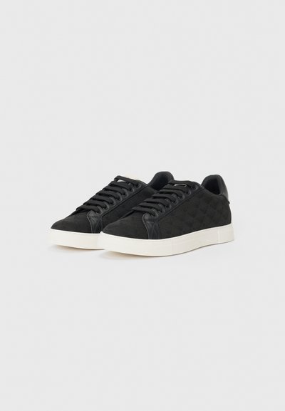 Baskets noires avec une surface texturée présentant un subtil motif à carreaux, une semelle en caoutchouc blanche et un design à lacets. Accents noirs lisses sur le talon.