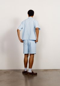 Lyseblå kortermet skjorte og matchende shorts, strukturerte stoffer, avslappet passform, kombinert med brune sko og hvite sokker. Enkelt design.