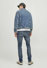 Chaleco de mezclilla en azul medio con un corte relajado, combinado con jeans azul oscuro. El chaleco presenta costuras sutiles y botones de metal.