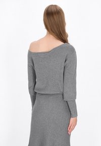 Pulover gri tricotat, cu umerii descoperiți, cu mâneci lungi și o siluetă scurtă. Textură moale și detaliu cu margine zimțată.