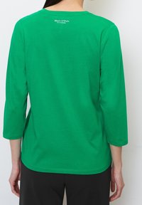 Grünes Baumwoll-T-Shirt mit langen Ärmeln und Rundhalsausschnitt. Verfügt über ein kleines Logo auf der Rückseite, eine glatte Textur und einen lockeren Schnitt.