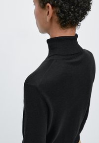 Czarny sweter z golfem z prążkowanym kołnierzem i bezszwowymi ramionami, prezentujący miękką fakturę i dopasowany krój. Widok od tyłu.