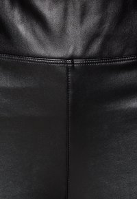 Black faux leather material with a smooth texture. Features a stitched seam along the center for structure.