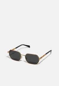 Goldene, metallische, achteckige Sonnenbrille mit dunklen Gläsern und schwarzen Plastikbügeln. Auffällige Kettendetails an den Schläfen.