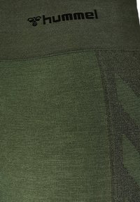 Mörkgröna träningsleggings med en texturerad stickning, en kontrasterande panel och en svart logotyp vid midjan, som visar en strömlinjeformad design.