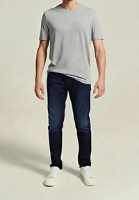 Camiseta gris de manga corta, vaqueros azul oscuro y zapatillas blancas. La camiseta tiene un cuello redondo; los vaqueros son ajustados y las zapatillas tienen detalles mínimos.