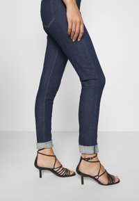 Svarta sandaletter med remmar och låg klack, matchat med mörkblå skinny jeans som har uppvikta fållar och kontrasterande sömmar.