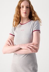 Siva rebrasta T-majica s kratkim rukavima, koja ima izrez u crveno-bijelim tonovima i izvezeni logo "Calvin Klein" na prsima.