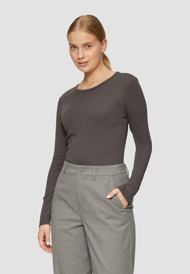 Langärmliges, dunkelgraues Oberteil aus weichem Material mit rundem Halsausschnitt. Kombiniert mit hoch taillierten grauen Hosen mit seitlichen Taschen.