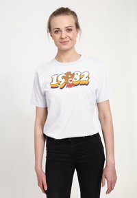 Weißes Baumwoll-T-Shirt mit einem bunten Grafikdesign, das "1982" und einen Bären auf Rollschuhen zeigt, vor einem neutralen Hintergrund.
