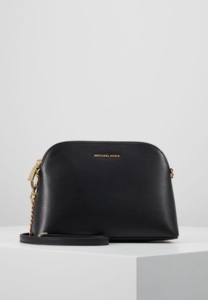 Czarna skórzana torebka na ramię Michael Kors z złotym łańcuszkiem i suwakiem, położona na białej powierzchni na tle w kolorze szarym.