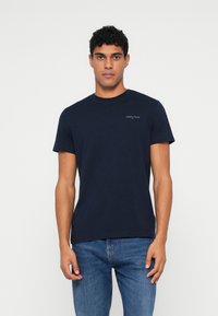 Μαρινί μπλουζάκι με στρόγγυλη λαιμόκοψη, κατασκευασμένο από βαμβάκι, με κοντά μανίκια και ένα μικρό λευκό λογότυπο στο στήθος. Λείο υλικό, χαλαρή εφαρμογή.