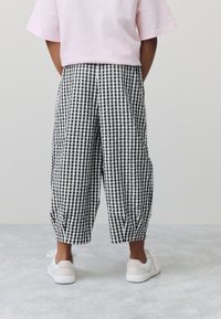 Schwarz-weiß karierte Gingham-Hosen mit weiter Passform, an den Knöcheln gerafft, kombiniert mit weißen Sneakern und einem pinkfarbenen, übergroßen T-Shirt.